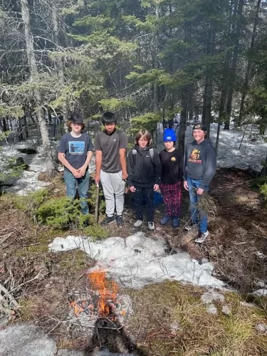 5 students stand together at a fire outdoors.