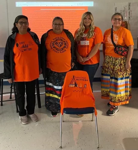 Four women pose wearing orange shirts