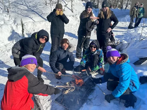 Group of students roasting hot dogs on a winter fire.