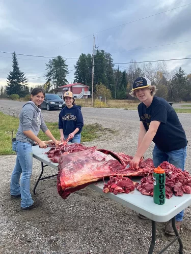 Three students butcher a moose on a table.