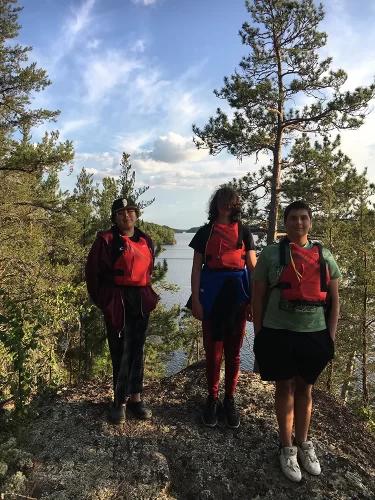 Three students pose wearing life jackets outdoors.
