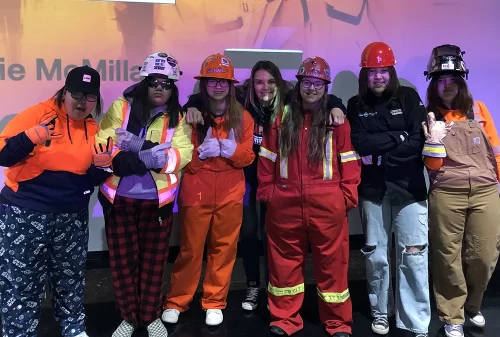 Young women in trades equipment pose for the camera.